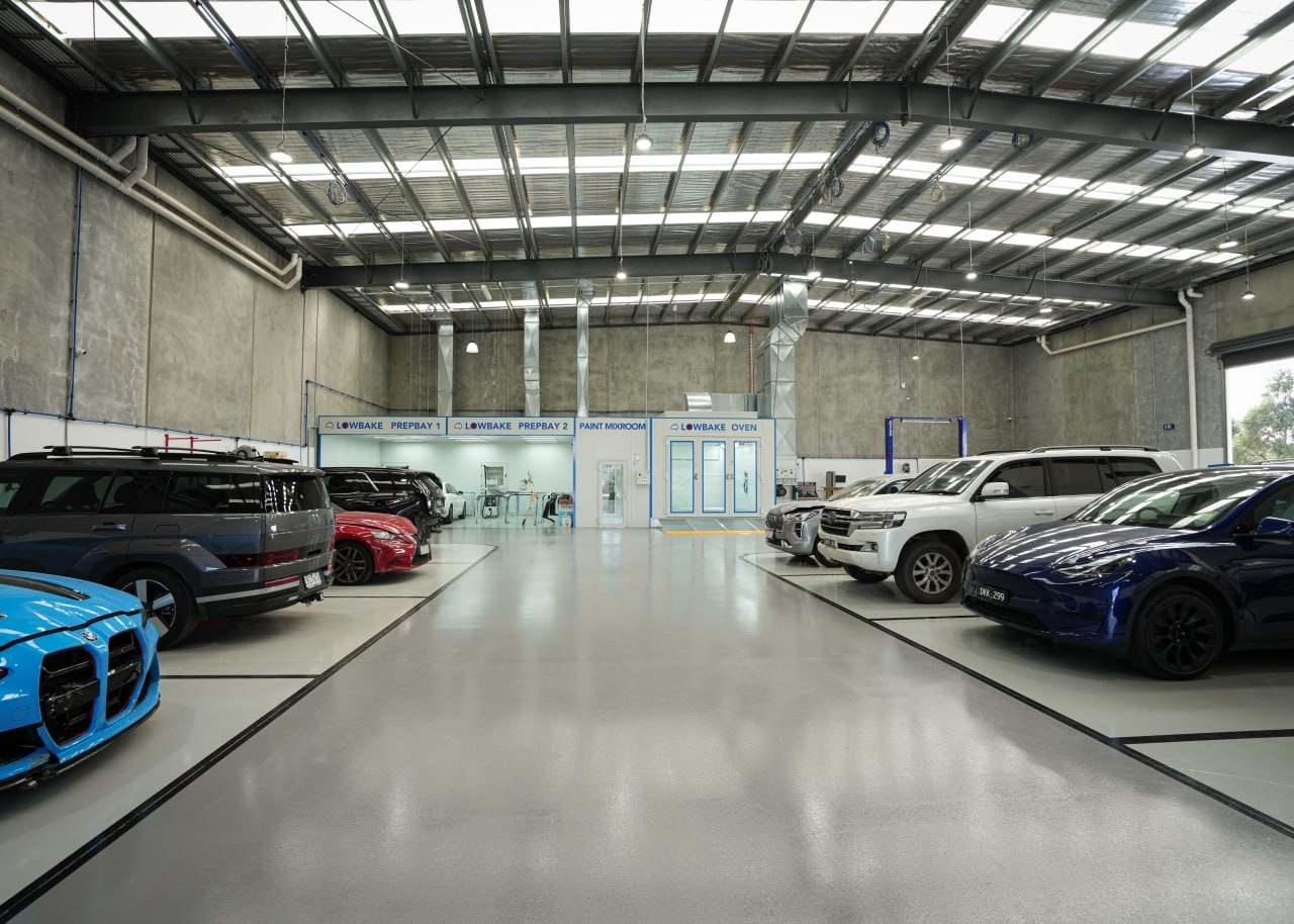 Vehicles inside the Vic Tic Panels workshop beside the LOWBAKE preparation bays and oven